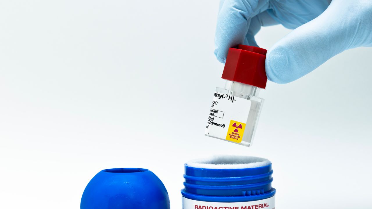 Gloved hand removing a vial of radioactive material from a shielded container